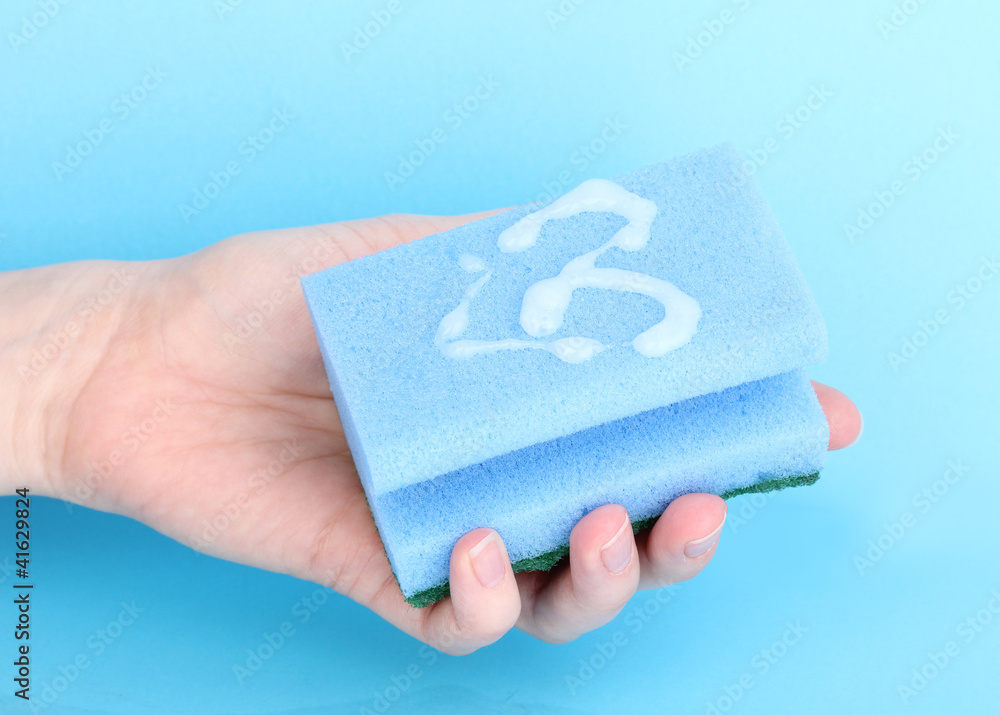 Sponge in hand with detergent on blue background