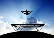 Silhouette Of Female Gymnast On Trampoline In Front Of Clouds