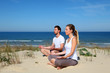 © goodluz - Couple doing yoga exercices on a sandy beach