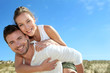 © goodluz - Man giving piggyback ride to girlfriend on a sand dune