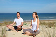 © goodluz - Couple doing yoga exercices on a sandy beach
