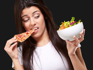 Wall Mural - portrait of young woman eating pizza and looking salad over blac