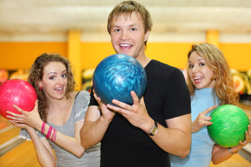 Young man and two happy girls hold balls in bowling club