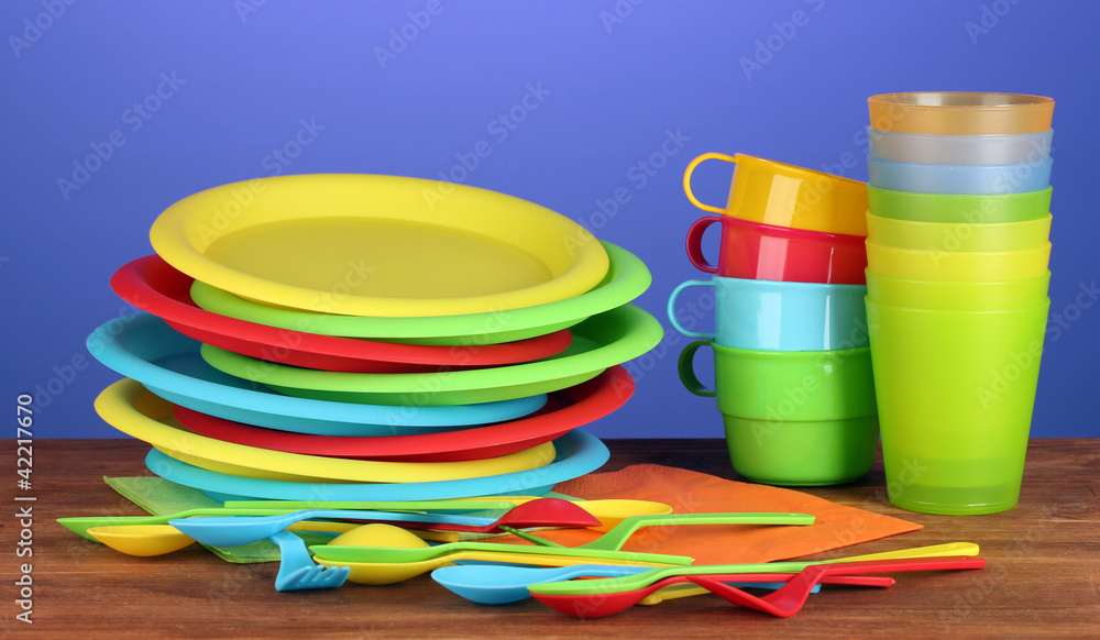 bright plastic tableware on wooden table on colorful background