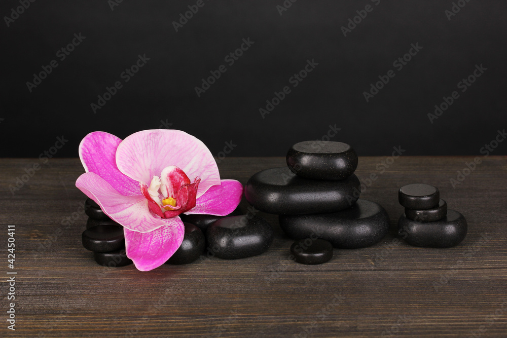 Spa stones with orchid flower on wooden table on grey background