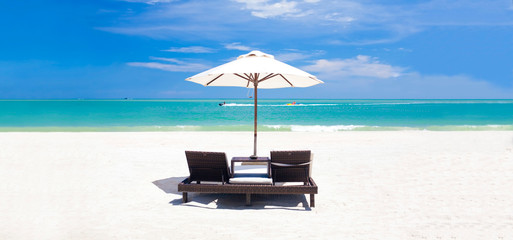 panoramic view of umbrella and two chairs on a tropical beach