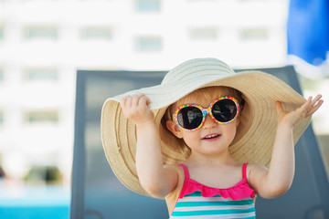 Wall Mural - Portrait of baby in hat and glasses sitting on sun bed