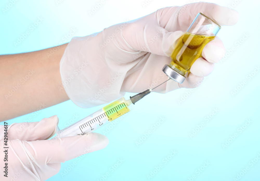 Syringe and medical ampoule in hands on blue background