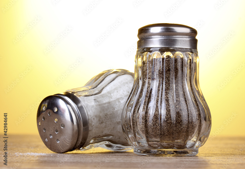 Salt and pepper mills on wooden table on yellow background