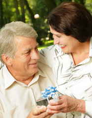 Mature happy smiling couple embracing in park with gift