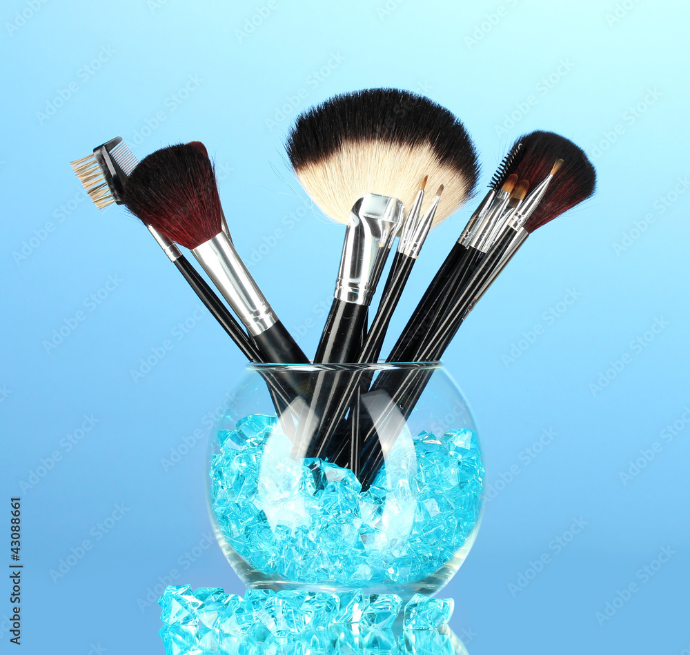Make-up brushes in a bowl with stones on blue background
