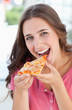 © WavebreakmediaMicro - A woman about to eat a piece of pizza as she looks at the camera