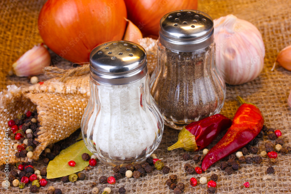 Salt and pepper mills and spices on burlap background