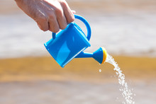 Hand Of A Man With A Watering Can On A Background Of Water