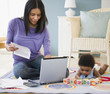 © JGI/Jamie Grill/Blend Images - African American mother working on laptop while baby plays on floor