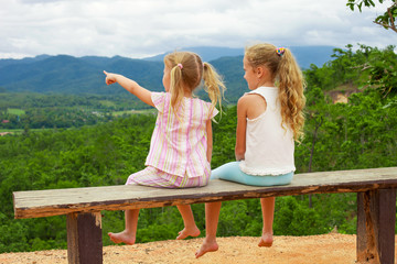 Two girls sit on the bench against the backdrop of the mountains