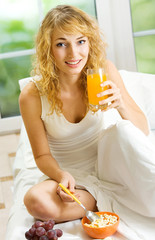 Wall Mural - Young woman with orange juice eating at home