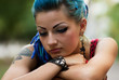 Portrait of beautiful diverse female with dyed blue hair and tattoo. Inclusive model with unique appearance posing outdoor in a cloudy day. Pretty punk girl with makeup and lip piercing
