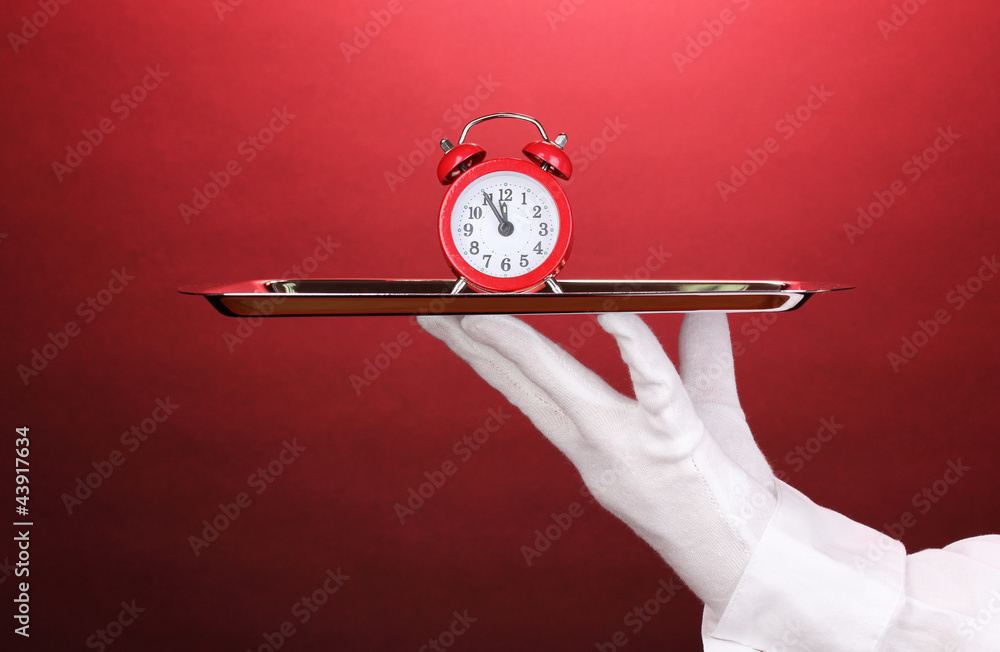 Hand in glove holding silver tray with alarm clock