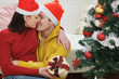 © Alliance - Romantic young couple with gift kissing near Christmas tree