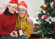 © Alliance - Happy young couple with gift sitting near Christmas tree