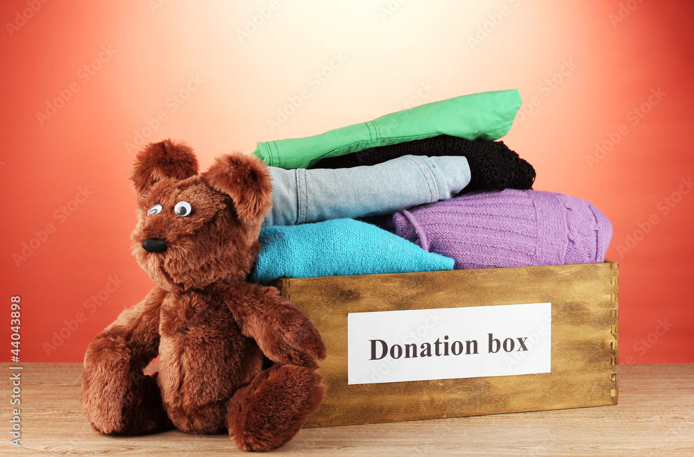Donation box with clothing on red background close-up