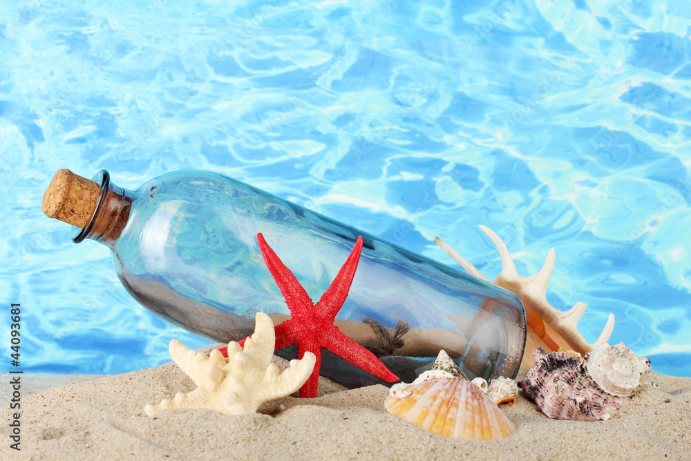Glass bottle with note inside on sand, on blue sea background