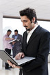 © Rehan Qureshi - young Businessman holding laptop with colleagues in background