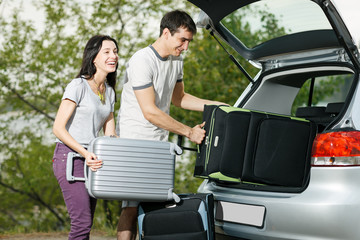 Happy couple going to vacations, loading their car boot