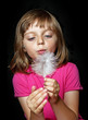little girl blowing into white feather on dark background