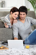 © auremar - Couple sat on couch with newspaper and laptop