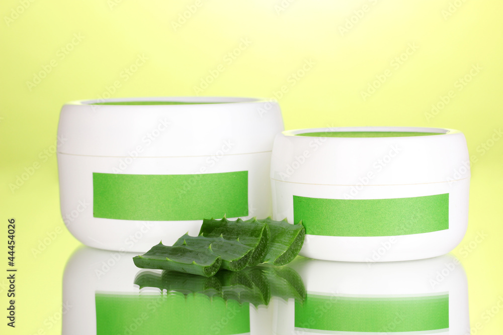 Jars of cream with aloe vera on green background