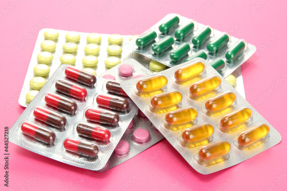 Capsules and pills packed in blisters, on pink background