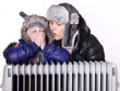 canvas print picture - Mother and daughter in warm winter coats leaning over a radiator