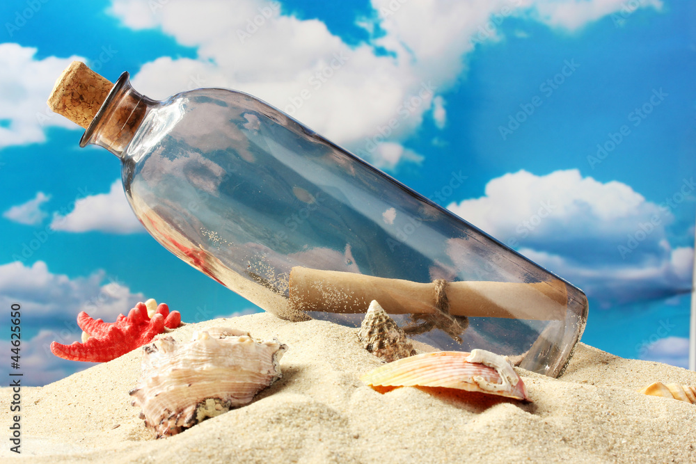 Glass bottle with note inside on sand, on blue sky background