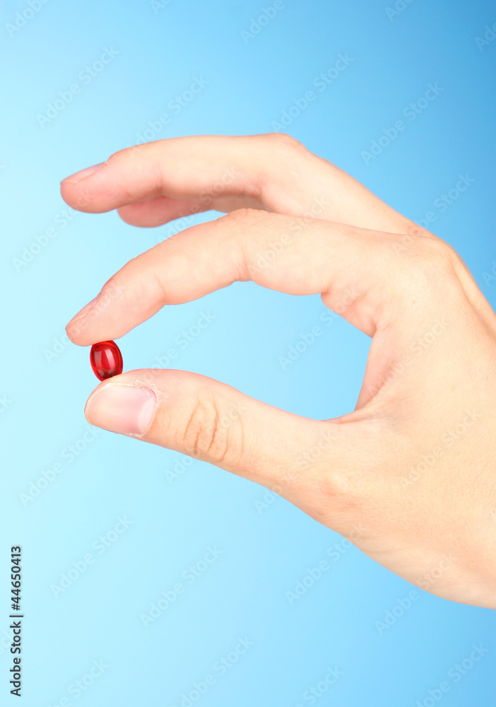 Woman's hand holding a red pill on blue background close-up