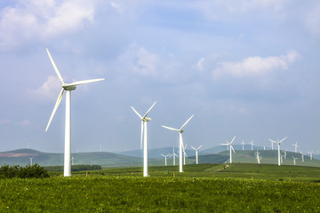 Wind turbine on the green grass over the blue clouded sky