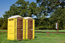 Two Yellow Portable Toilets At A Park