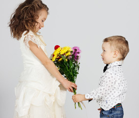 Smiling boy presenting bunch of colored flowers to charming girl