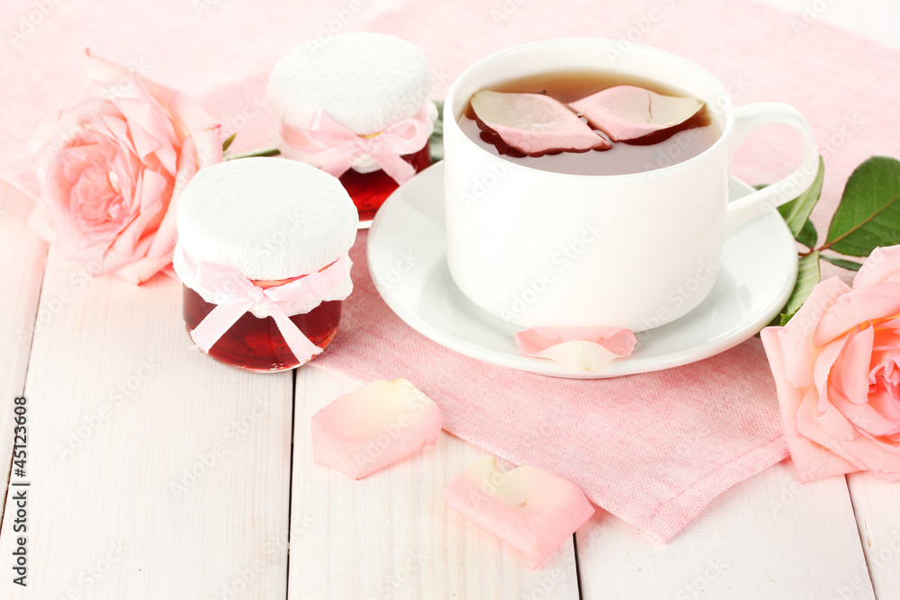 cup of tea with roses and jam on white wooden table