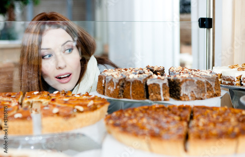 Fotografie, Obraz Woman in scarf looking at the bakery glass case