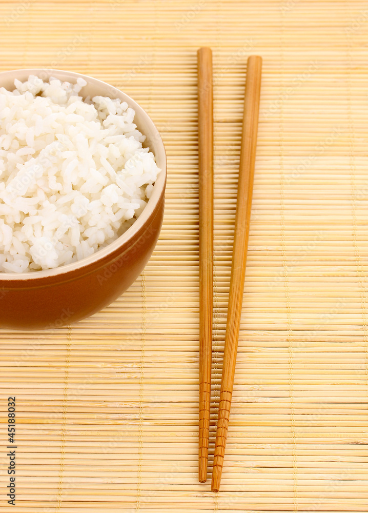 Bowl of rice and chopsticks on bamboo mat