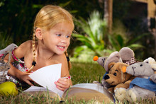 девочка читает книгу с игрушками на природе