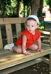 Fun baby sitting on bench with surprising looking face in beauti