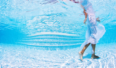 Underwater woman portrait with white dress in swimming pool.