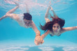 Underwater couple holding hands in swimming pool.