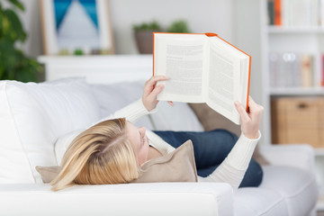 blonde frau liest ein buch auf dem sofa