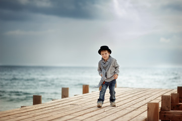 Stylish boy in a hat standing on a wooden bridge on the backgrou