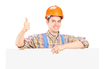 Wall Mural - Happy male construction worker posing behind a panel giving thum