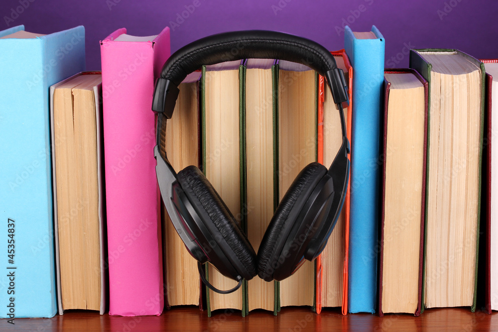 Headphones on books on wooden table on purple background